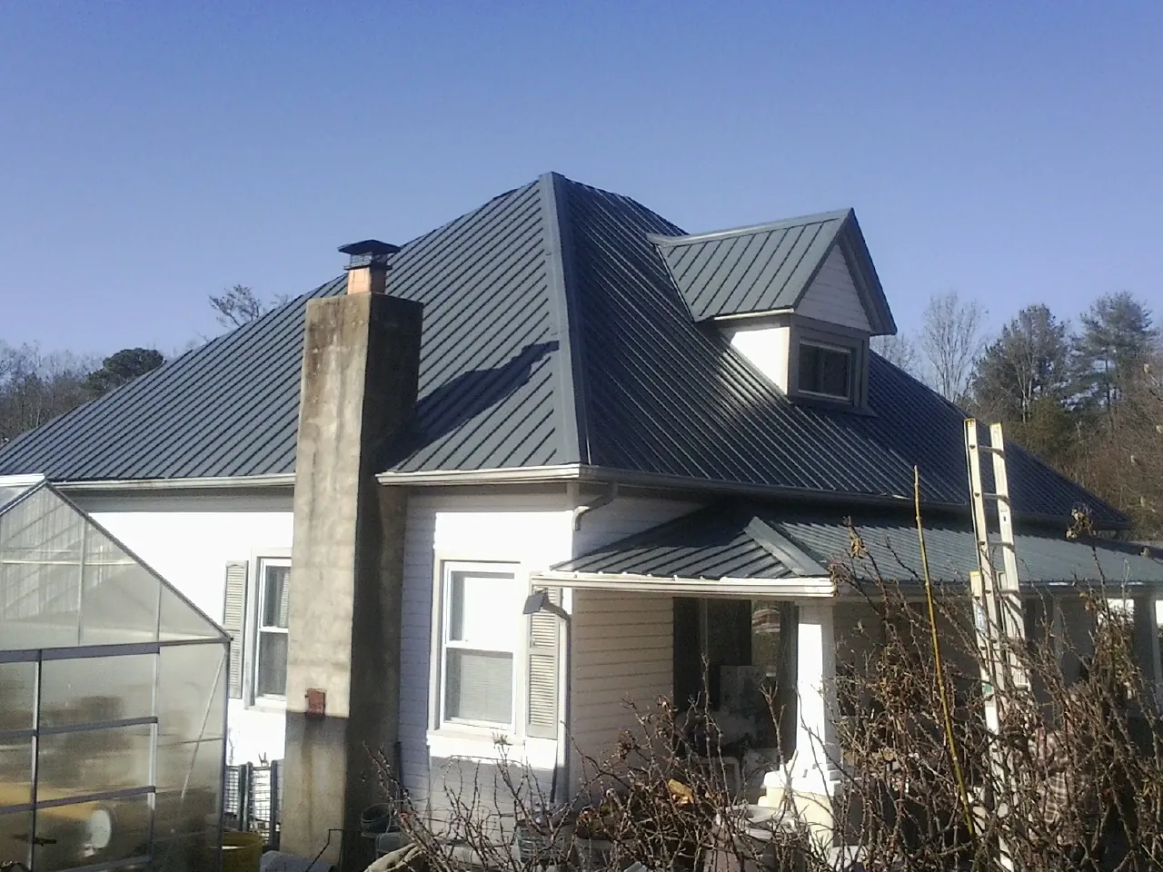 Dark blue standing seam metal roof on a white farmhouse with dormer — Slate & Tile Roof Repair by Roofing Brothers in Stryker
