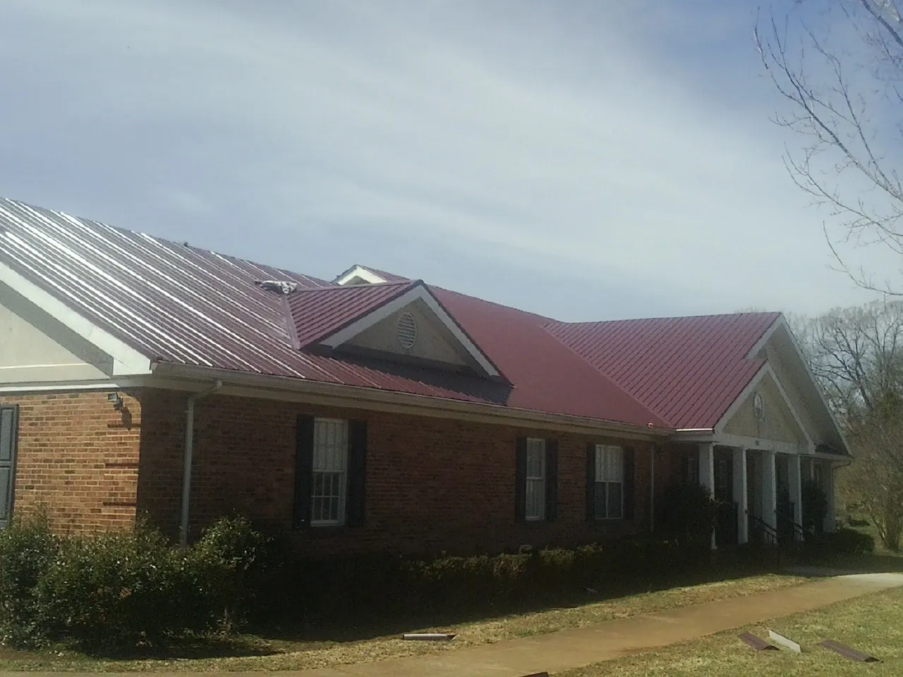 Red metal roof with gabled entries on a long brick building, from a Hail Damage Roof Repair job in Stryker