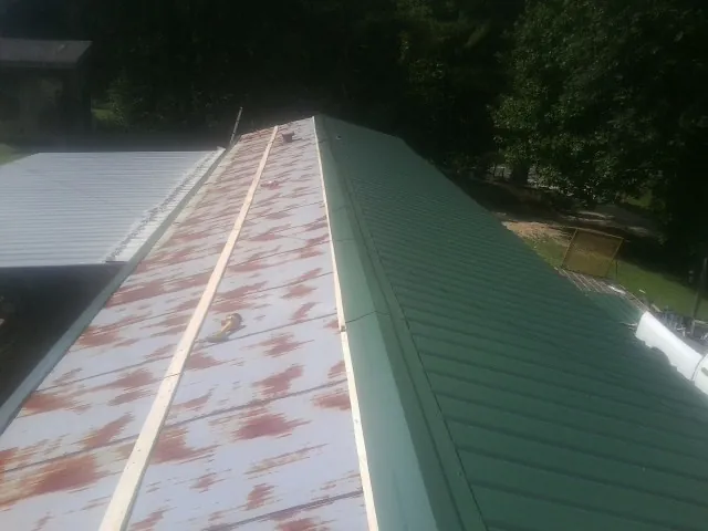 Old rusted panels beside newly installed green metal roofing — Wind Damage Roof Repair by Roofing Brothers in Stryker