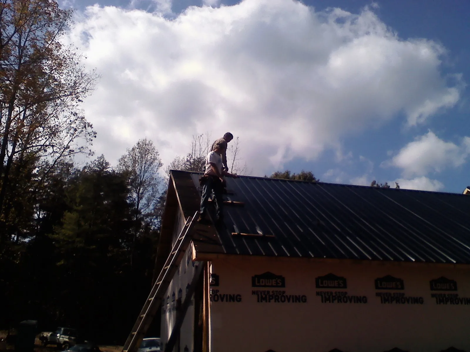 Roofer fastening dark metal panels high against a cloudy sky, from a Roof Inspection job in Stryker